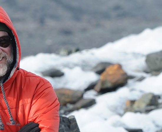 A backpacker wearing a hooded down jacket hiking across Malaspina Glacier, Wrangell-St. Elias National Park, Alaska.