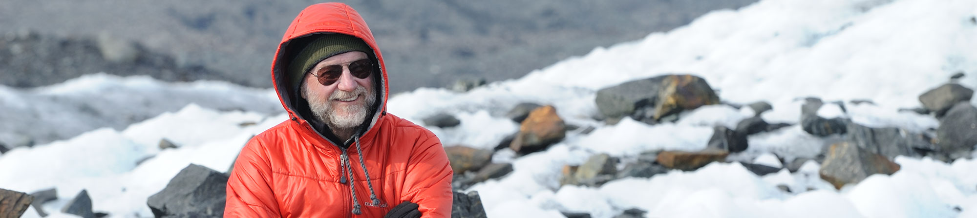 A backpacker wearing a hooded down jacket hiking across Malaspina Glacier, Wrangell-St. Elias National Park, Alaska.