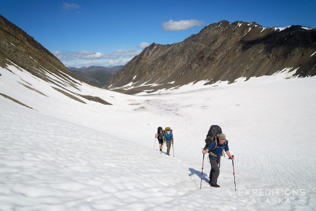 Backpackers traversing a snow-covered alpine pass in Alaska.