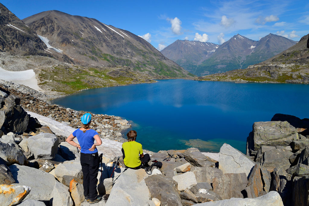 Hikers overlook on alpine lake Chugach mountains, Seven Pass Route, backpacking trip, Wrangell - St Elias National Park, Alaska.