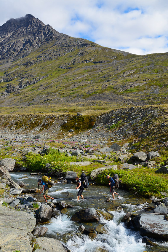 Hikers crossing a stream on Southern traverse backpacking route in Wrangell-St. Elias National Park, Alaska.
