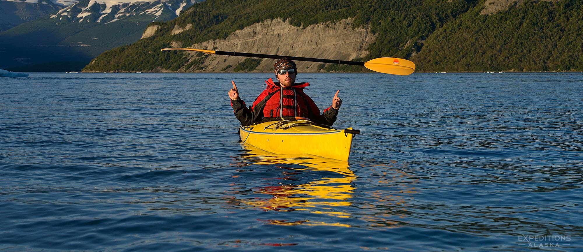 Sea kayaking, a kayaker with a paddle on his head, and Mt. St. Elias from Icy Bay, Alaska.